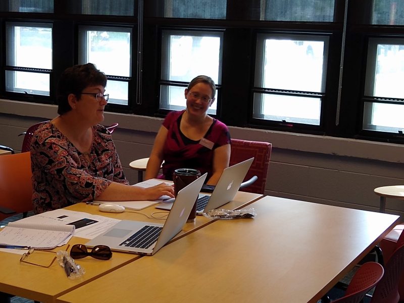 two women. One woman with hand on laptop keyboard while second woman looks on smiling.