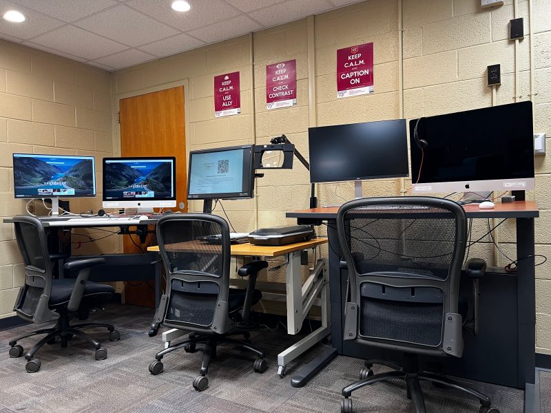 Three sit-to-stand tables with ergonomic chairs, the right and left desks have a large display and an Apple iMac desktop computer. The middle one also has a video magnifier and scanner..