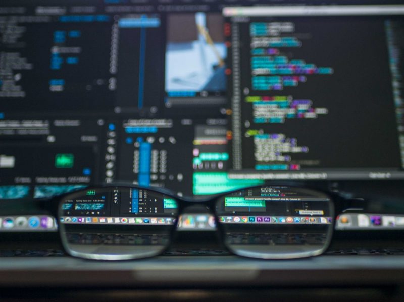 out-of-focus view of computer screens displaying code, with reading glasses showing a clearer view